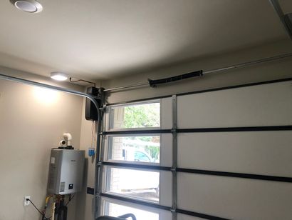 Garage interior with a closed sectional door, window, wall-mounted opener, and utility box.