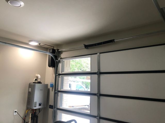 Garage interior with a closed sectional door, window, wall-mounted opener, and utility box.