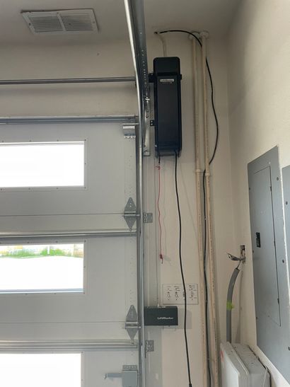 Garage wall with an open door opener, electrical panel, and exposed wires.