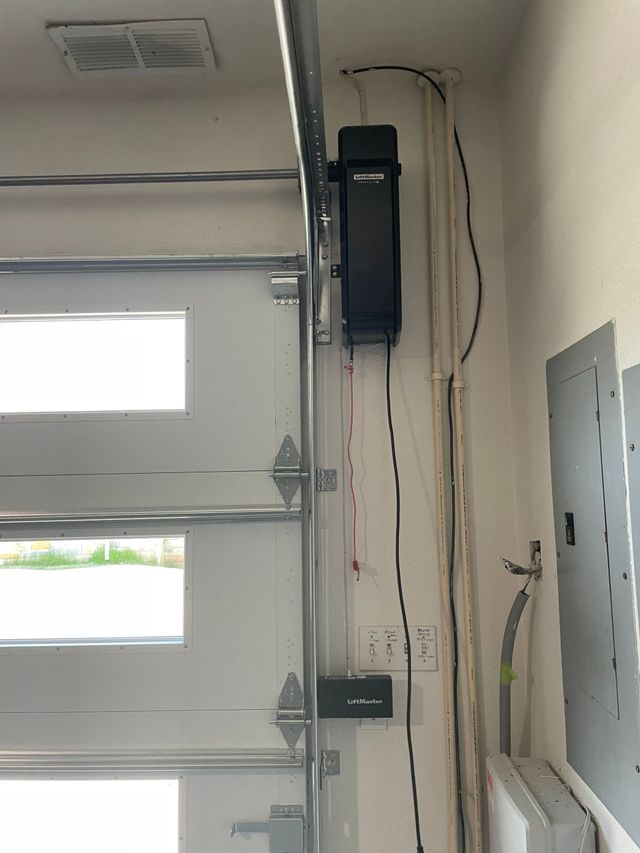 Garage wall with an open door opener, electrical panel, and exposed wires.