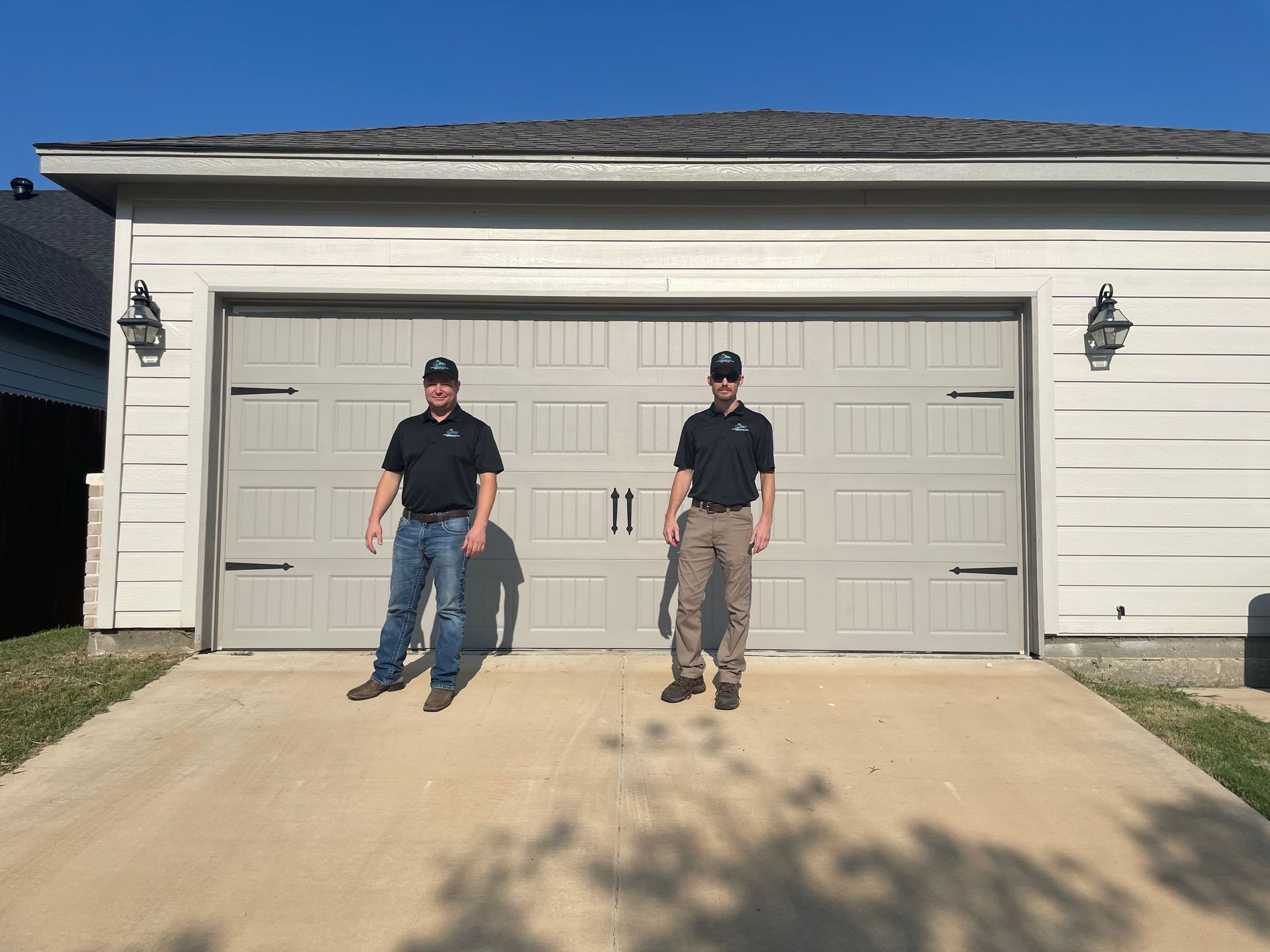 Two men standing in front of a beige garage with a double door and concrete driveway