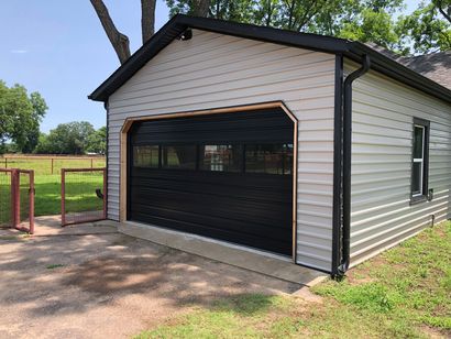 Detached light-gray garage with black trim and open door in a grassy yard