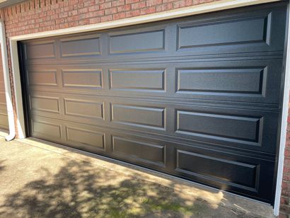 Black paneled garage door in a brick wall, lit by sunlight.