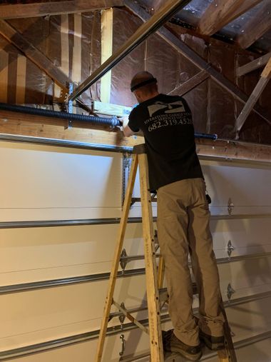 Worker on a ladder inspecting exposed attic framing and ductwork inside a house.