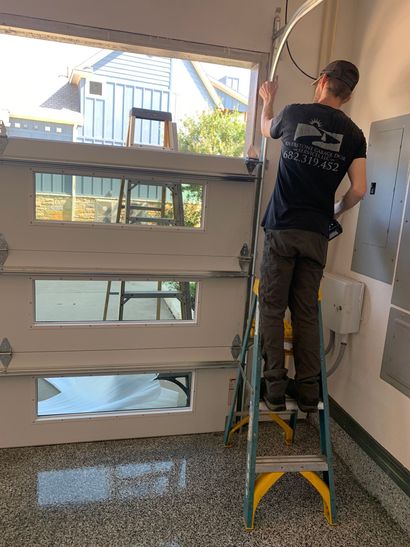 Person standing on a ladder installing a large window in a bright room