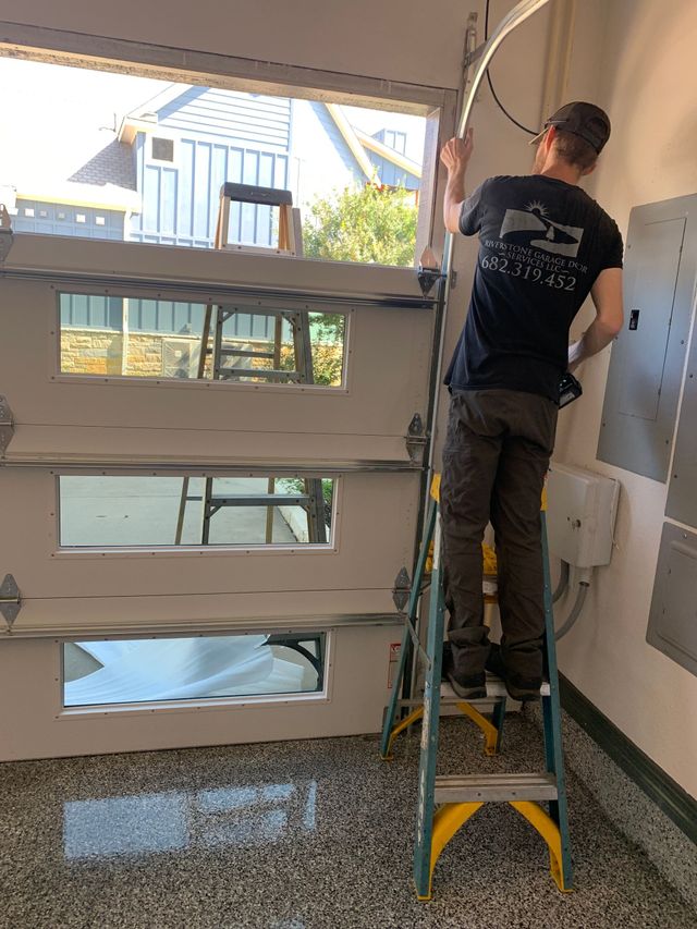 Person standing on a ladder installing a large window in a bright room