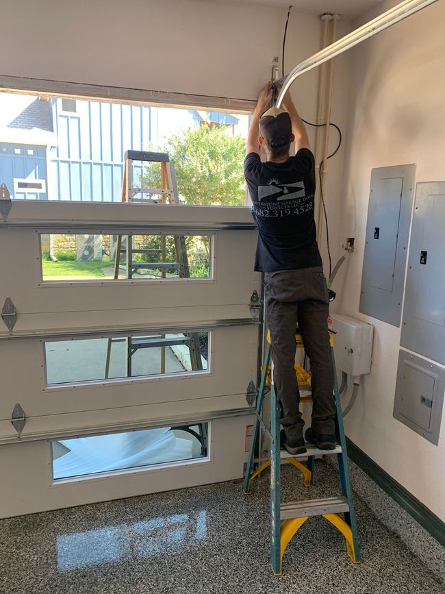 Person on a ladder installing a ceiling fixture in a bright room with large windows