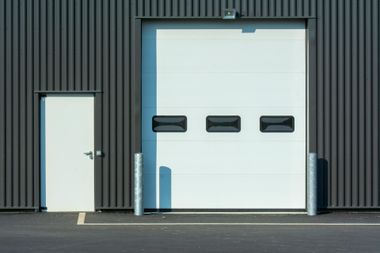 Open garage door corner with metal tracks, insulation, and daylight outside