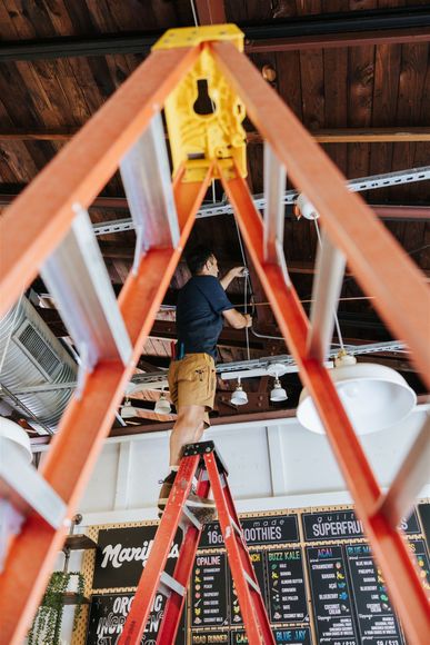 A person stands on a red ladder in a room with a rustic ceiling, performing maintenance work on the overhead lights.