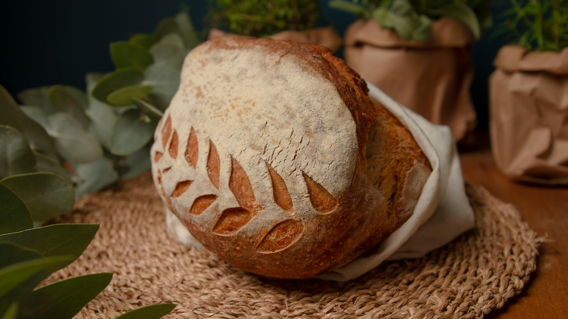Loaf of bread with leaf design, wrapped in cloth, on a woven mat.