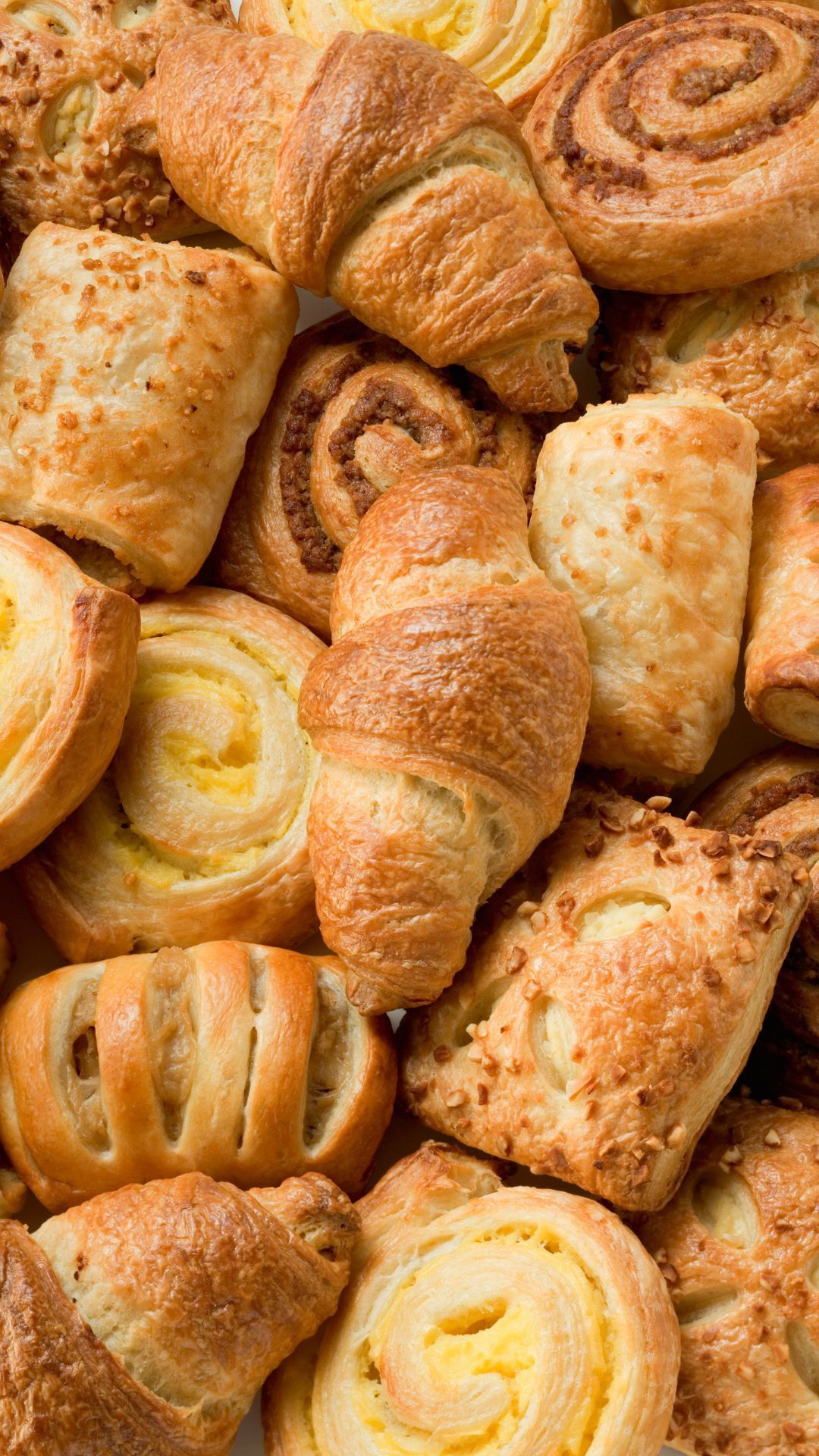 Assortment of golden-brown pastries: croissants, cinnamon rolls, and filled puff pastries.