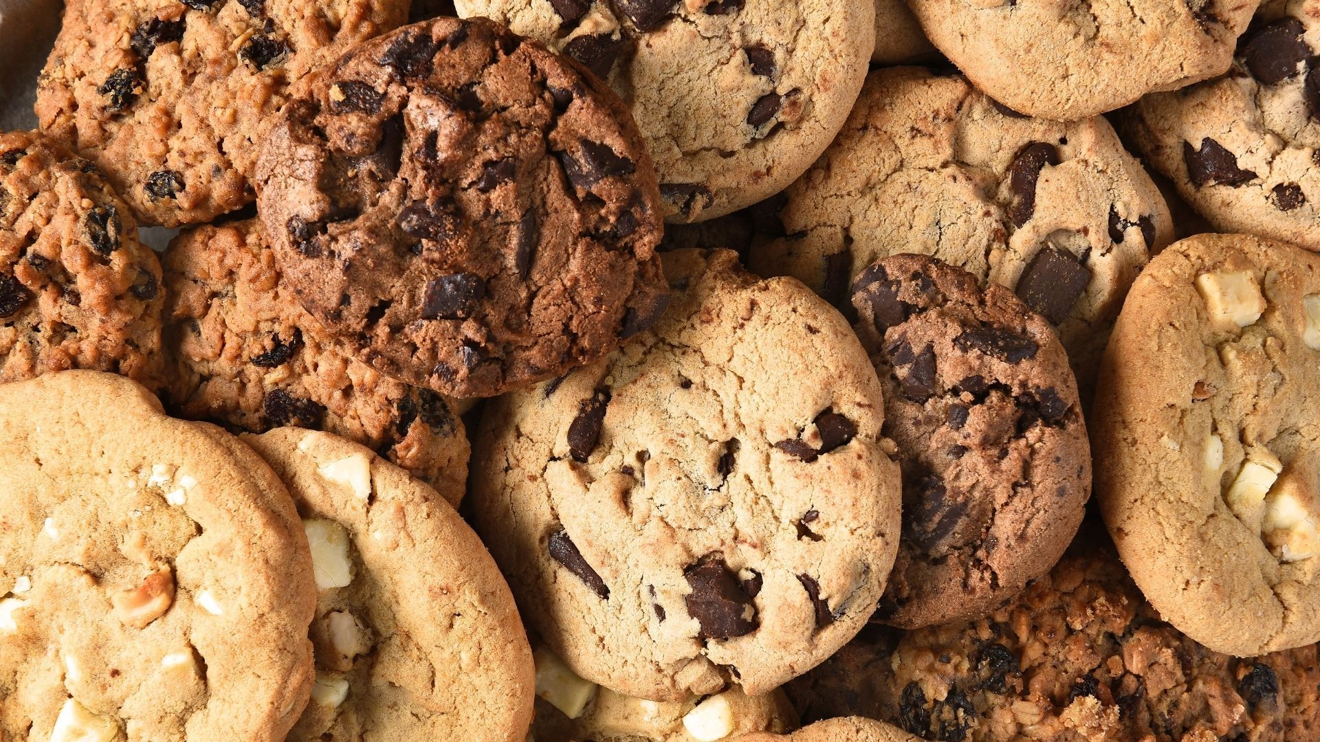 Close-up of a pile of various chocolate chip cookies, with light brown and dark chocolate chips.