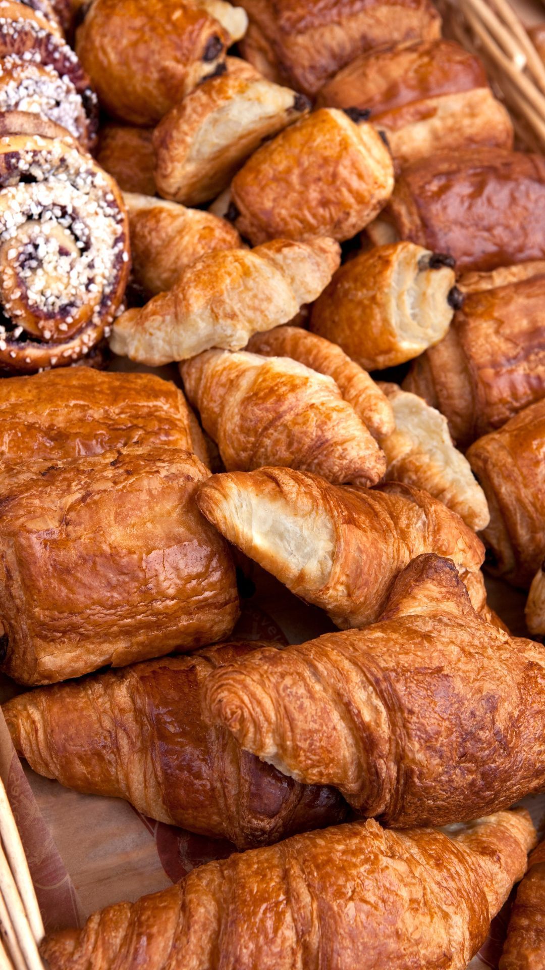 Assortment of baked pastries, including croissants and pain au chocolat, in a bakery display.