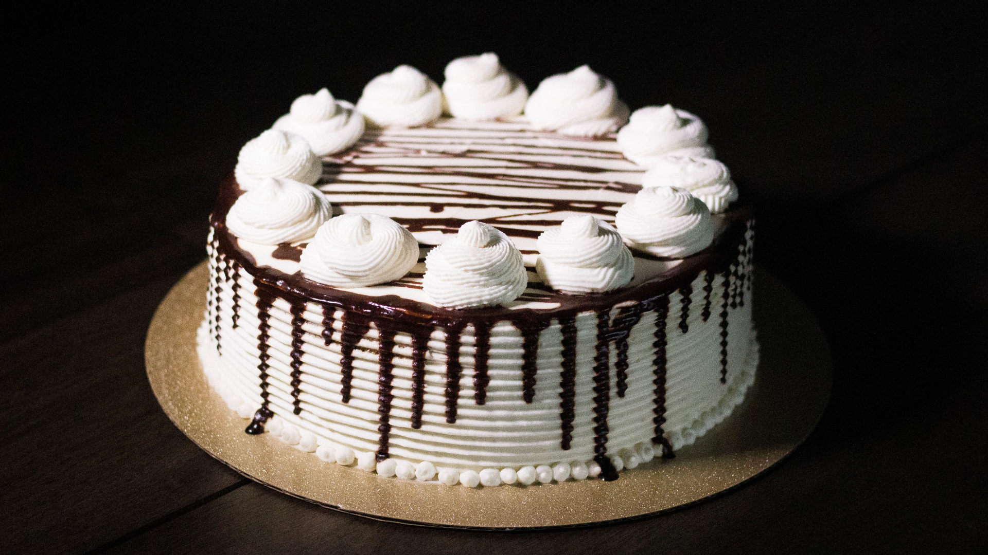White frosted cake with chocolate drizzle and whipped cream swirls.