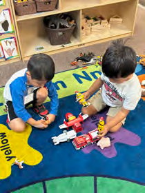 Two young boys are playing with toys on the floor in a classroom.