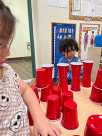 A little girl is playing with red cups on a table.