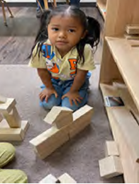 A little girl is sitting on the floor playing with wooden blocks.