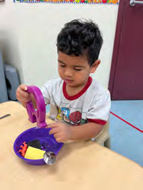 A young boy is sitting at a table playing with a purple toy.