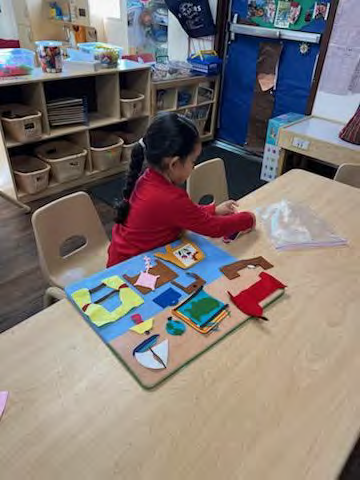 A little girl is sitting at a table playing with a felt board.