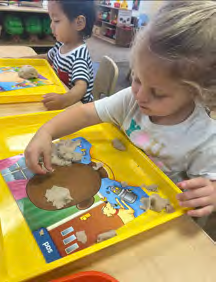 A little girl is playing with clay on a yellow tray.