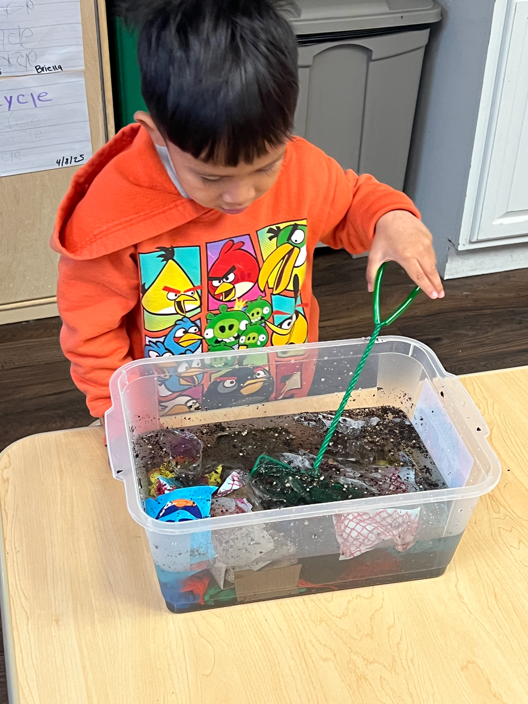 A young boy is playing with a plastic container on a table.