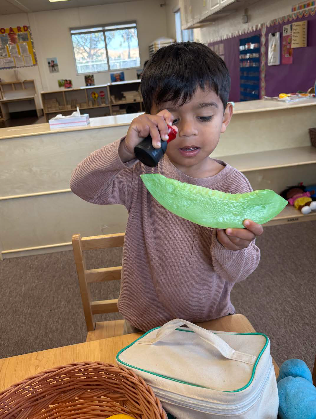 A young boy is sitting at a table holding a piece of green paper.