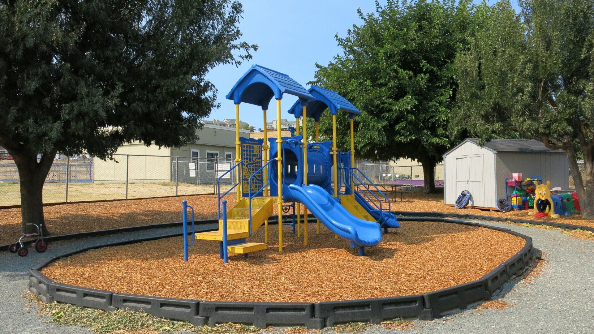 A blue and yellow playground with a slide and a shed in the background.