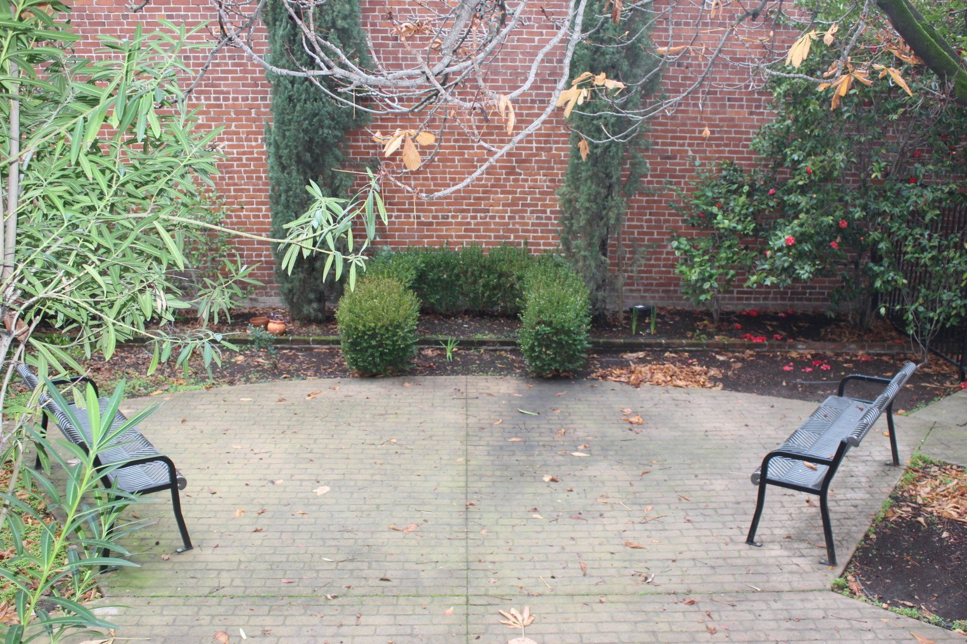 Two benches are sitting on a concrete patio in front of a brick wall.
