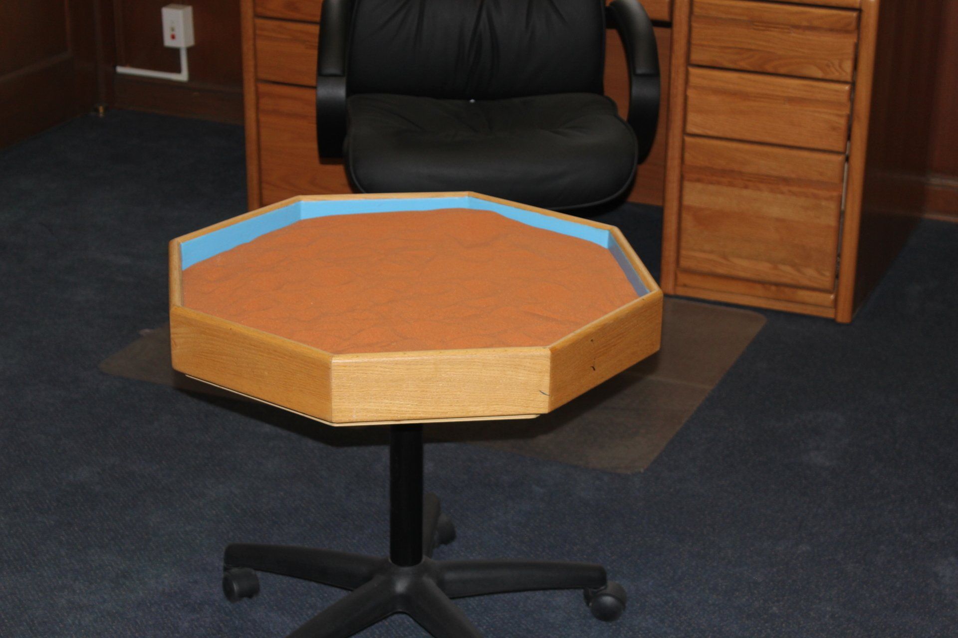 A black chair sits next to a wooden desk with drawers