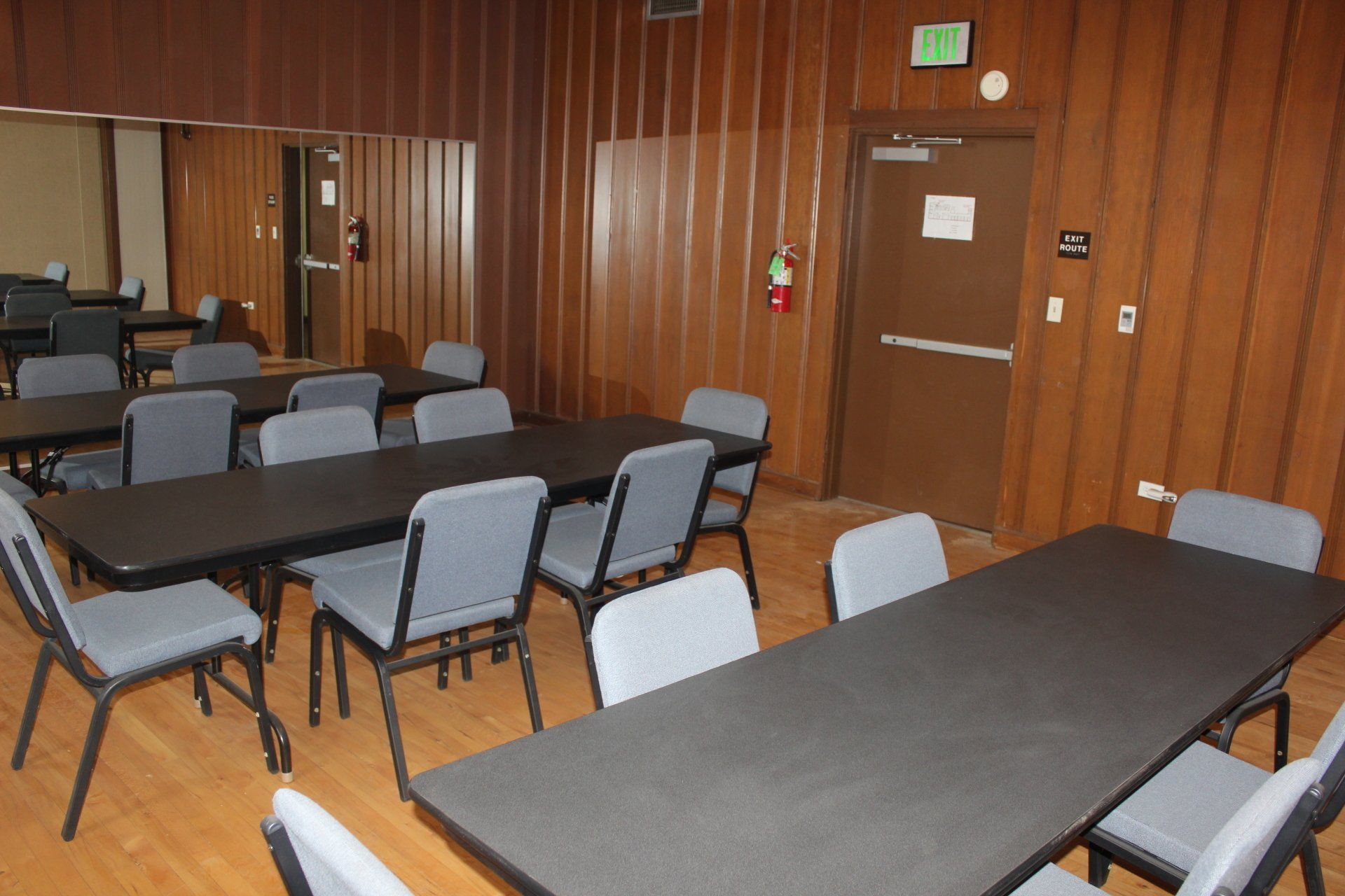 A room with tables and chairs and an exit sign on the wall