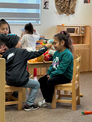 A group of children are sitting at tables and chairs in a classroom.