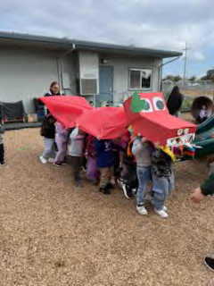 A group of children are playing with a red dragon costume.