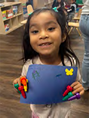 A little girl is holding a piece of paper with crayons on it.
