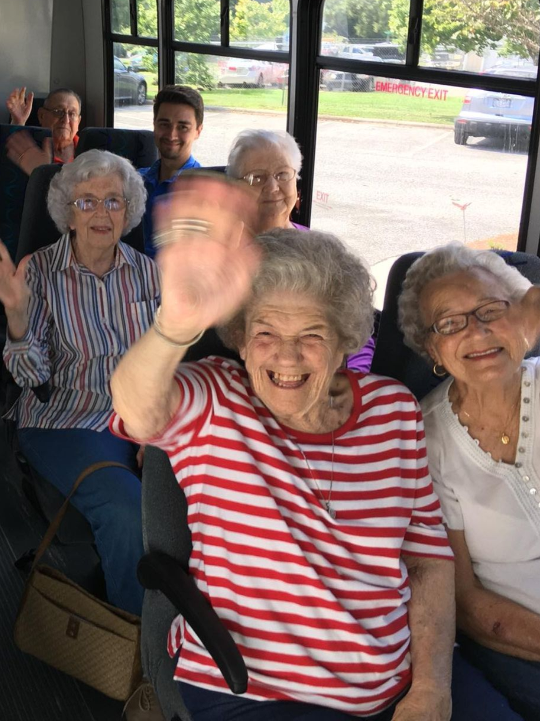 Group of people waving from inside a bus.  Independent senior living community near Raleigh, NC.