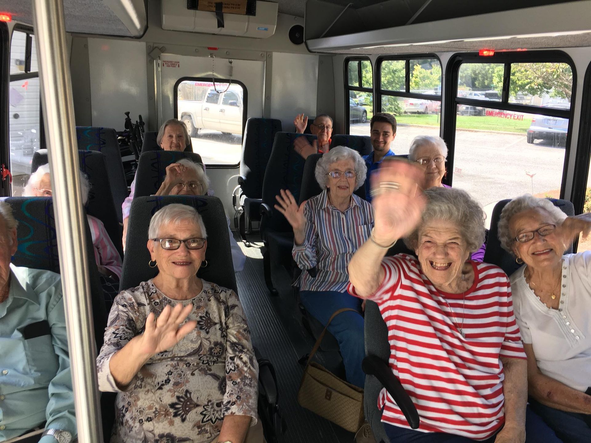 A group of elderly people are sitting on a bus waving.
