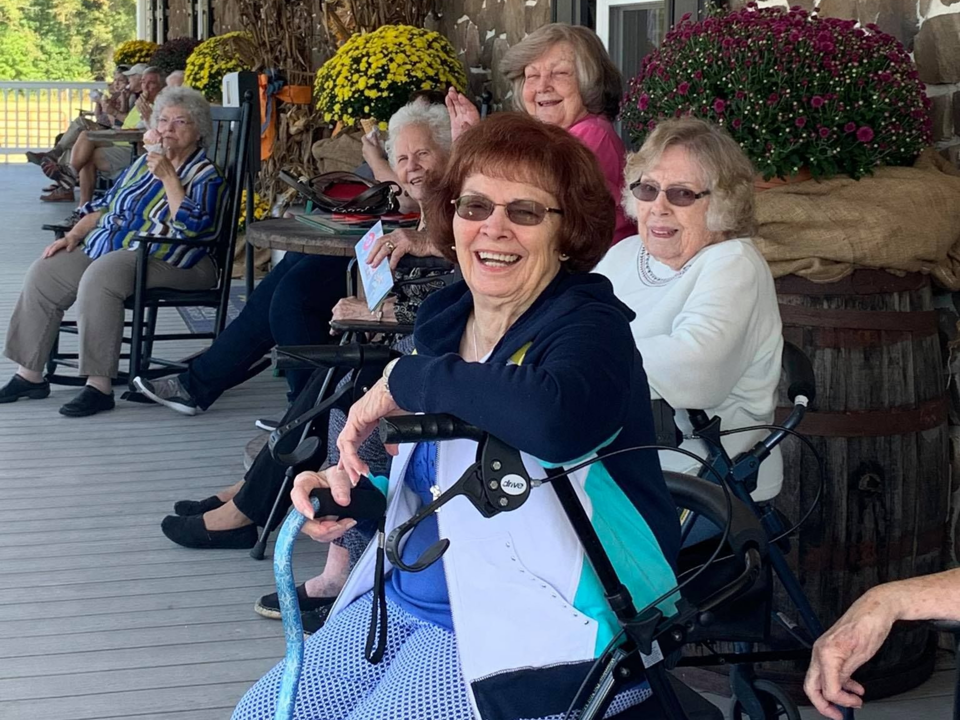 Group of senior citizens sitting on a porch. Some use walkers, enjoying the day. Flowers and decorations are visible. Senior retirement community near Goldsboro NC.