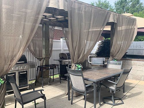 A patio with a table and chairs under a pergola with curtains.