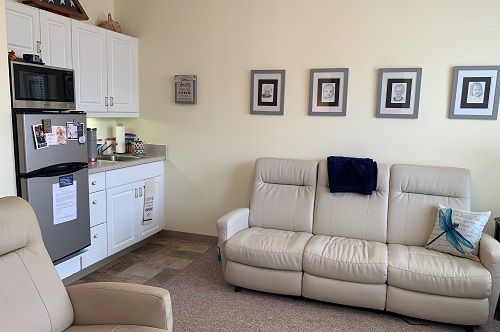 A living room with a couch , chair , refrigerator and microwave.