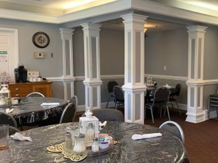 Dining room with round tables, black chairs, gray walls, and white columns.  Independent senior living community near Greenville, NC.