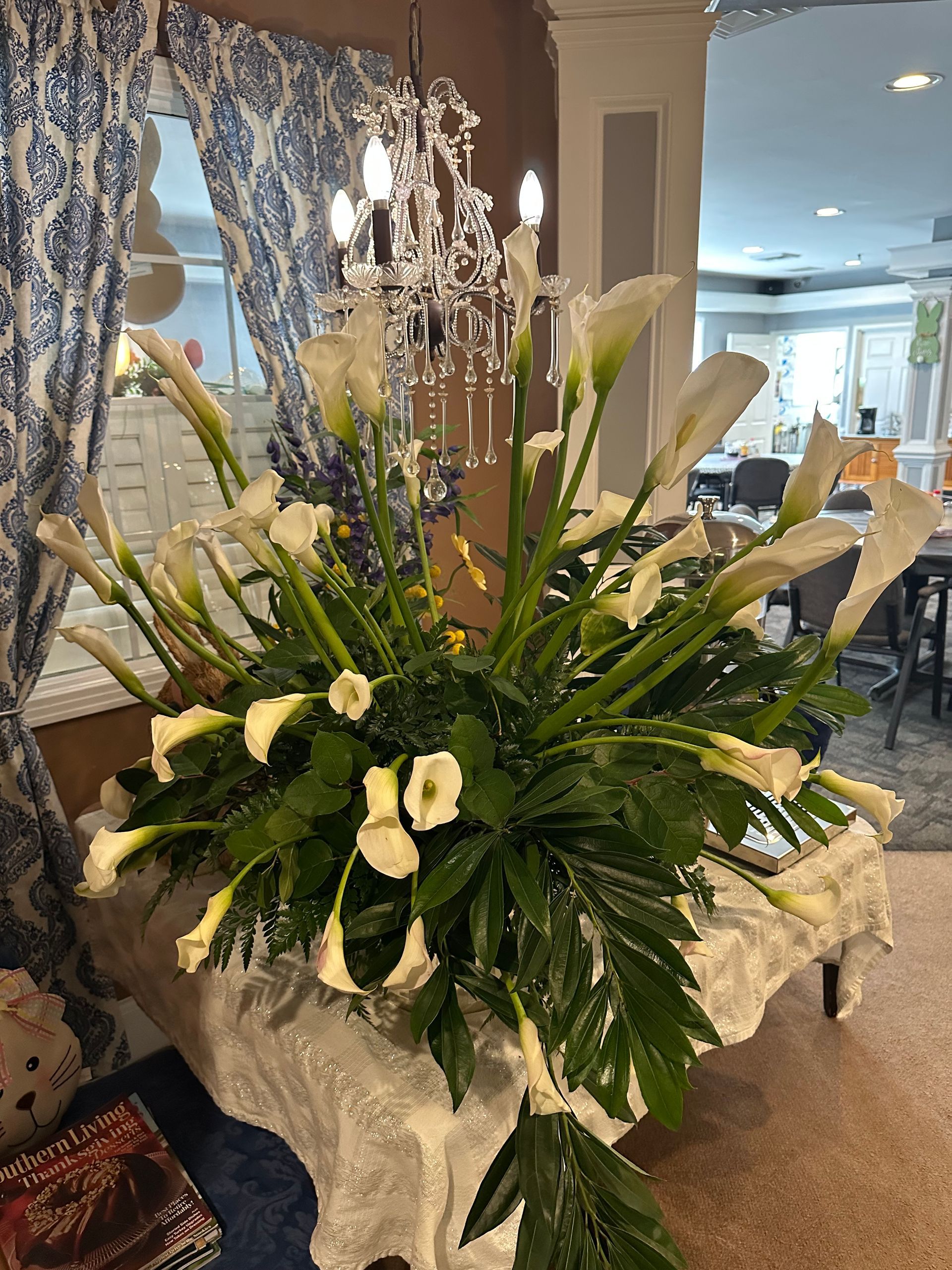 A large bouquet of white flowers is sitting on a table in front of a chandelier.