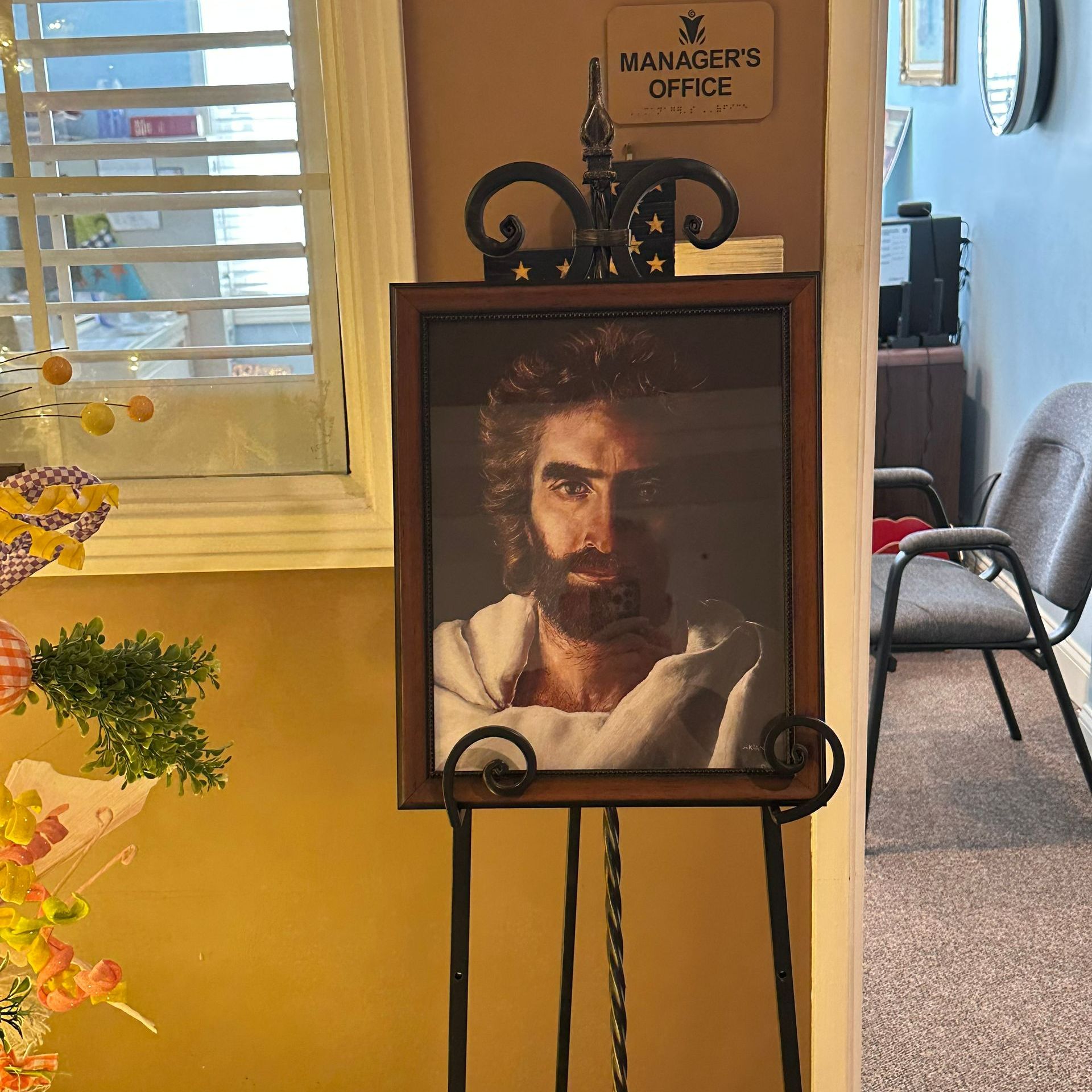 A picture of a man with a beard is on an easel in front of a sign that says manager 's office
