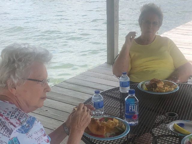 Two women are sitting at a table eating food and drinking fiji water.