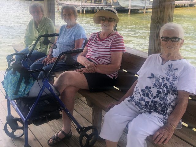 A group of older women are sitting on a bench by the water.