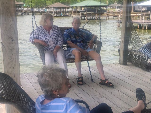 A man and two women are sitting on a swing overlooking a body of water.