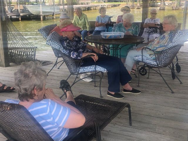 A group of older women are sitting around a table on a dock.