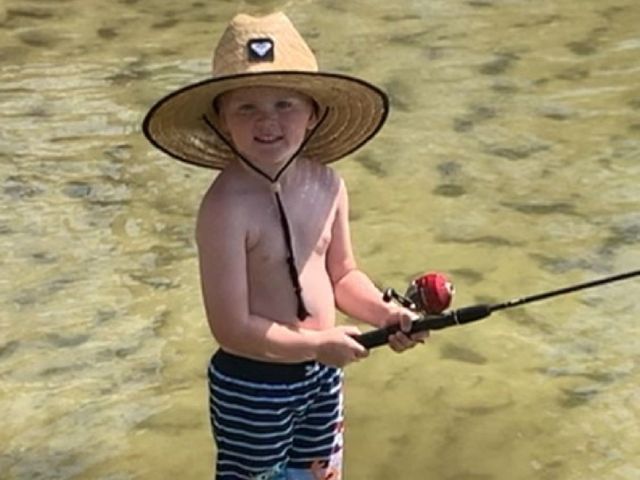 A young boy in a straw hat is holding a fishing rod in the water.