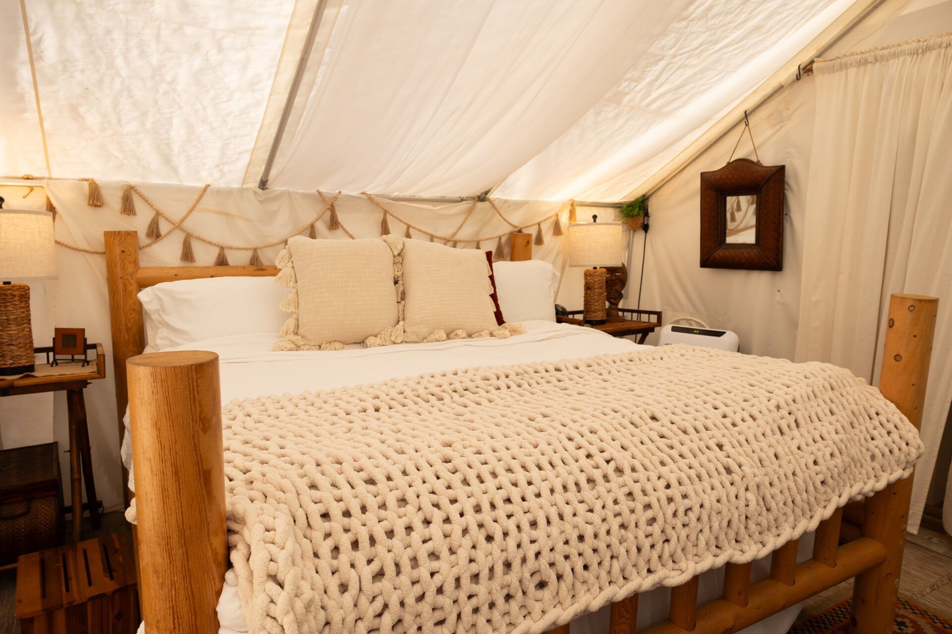 Cozy bed in a canvas tent with cream bedding, wooden posts, and warm lantern lighting