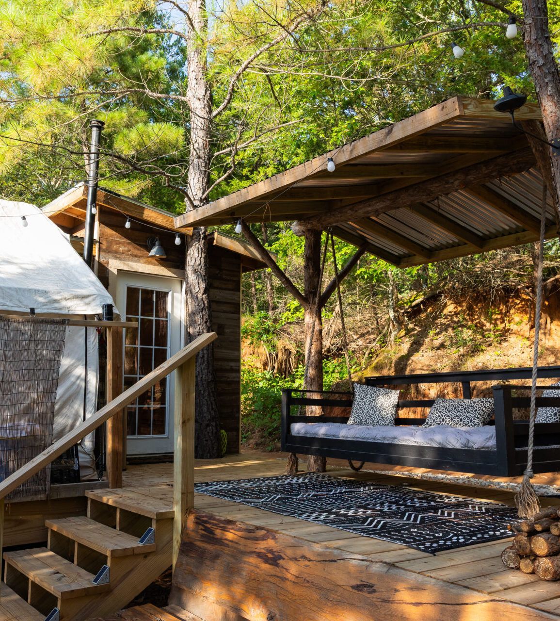 Rustic outdoor cabin porch with steps, covered seating, and trees in a wooded setting