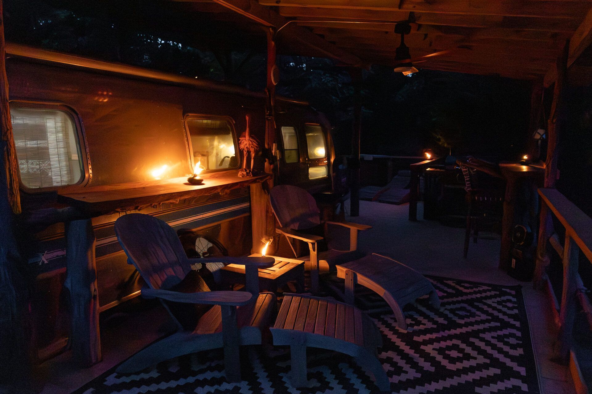 Cozy cabin porch at dusk with glowing lanterns, wooden chairs, and patterned rug under warm orange light