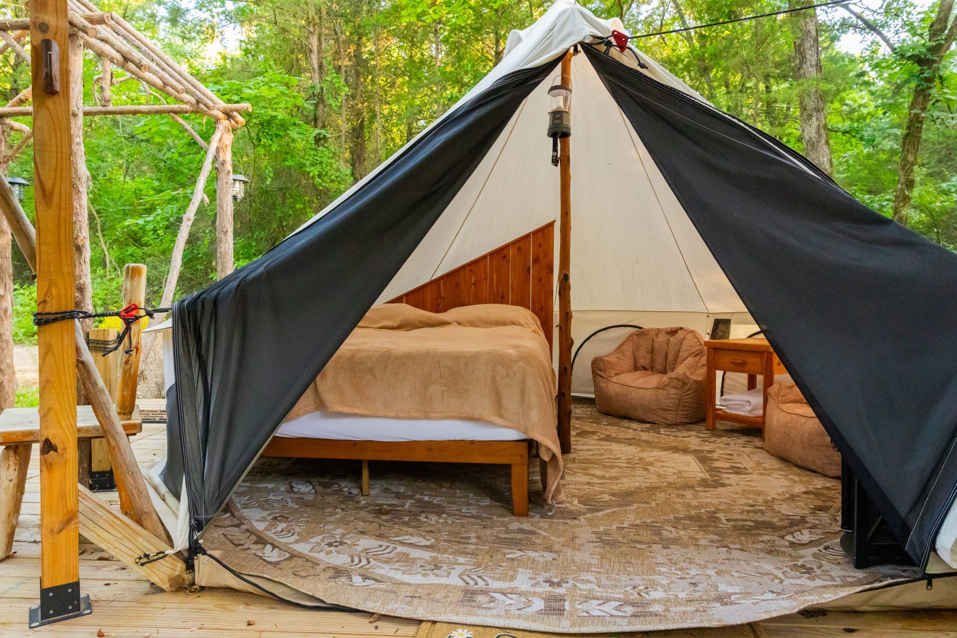 Small glamping tent with bed and seating on a wooden deck in a lush outdoor setting